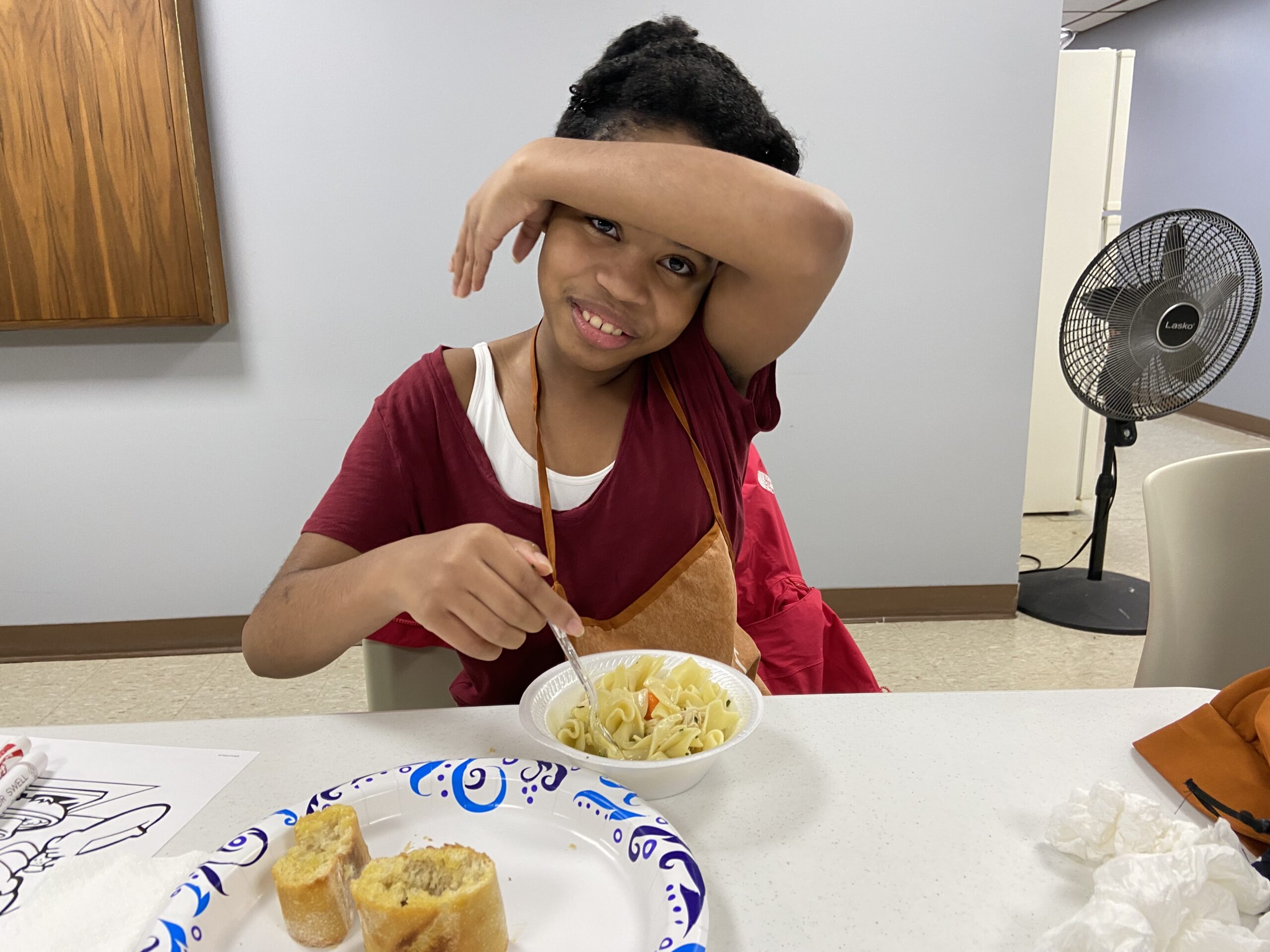 A young girl sits at a table about to eat the bread and pasta that is in front of her. This activity was done as a part of the junior chiefs program.